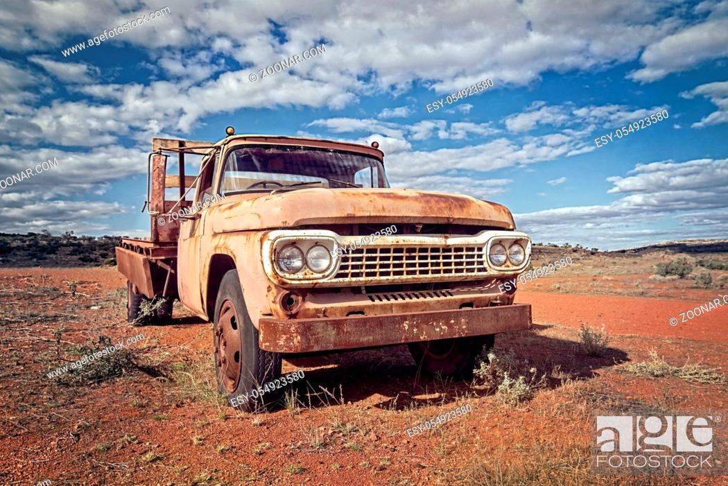 Stock Photo: Australia – Outback desert with an old vintage abandoned car near the track under cloudy sky.