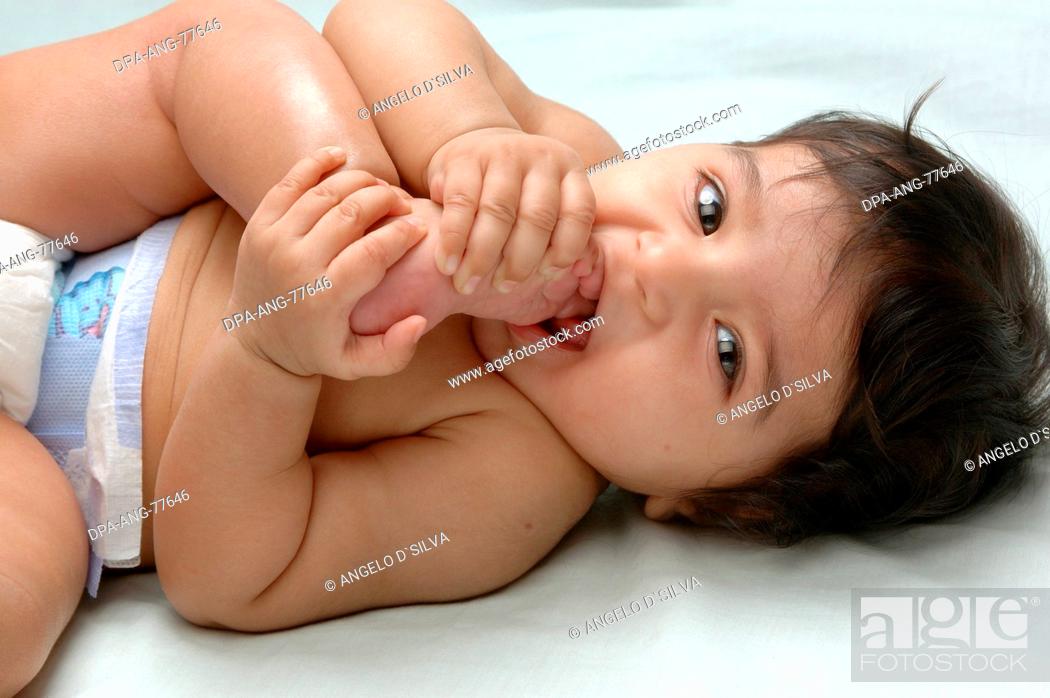 Stock Photo: Young baby Indian girl in diapers ; 4 months old ; Holding her feet putting her toe in the mouth and smiling ; Model Release 468.