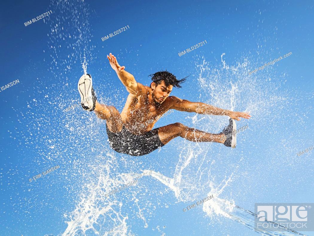 Stock Photo: Water spraying on jumping Hispanic man.