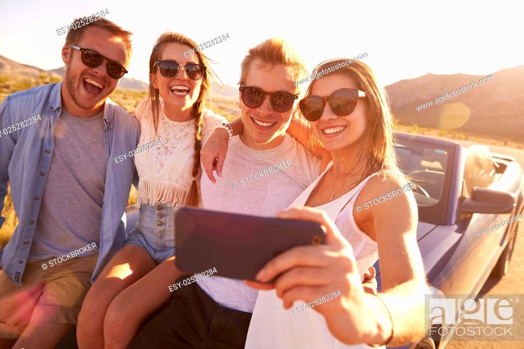 Stock Photo: Friends On Road Trip Sit On Convertible Car Taking Selfie.