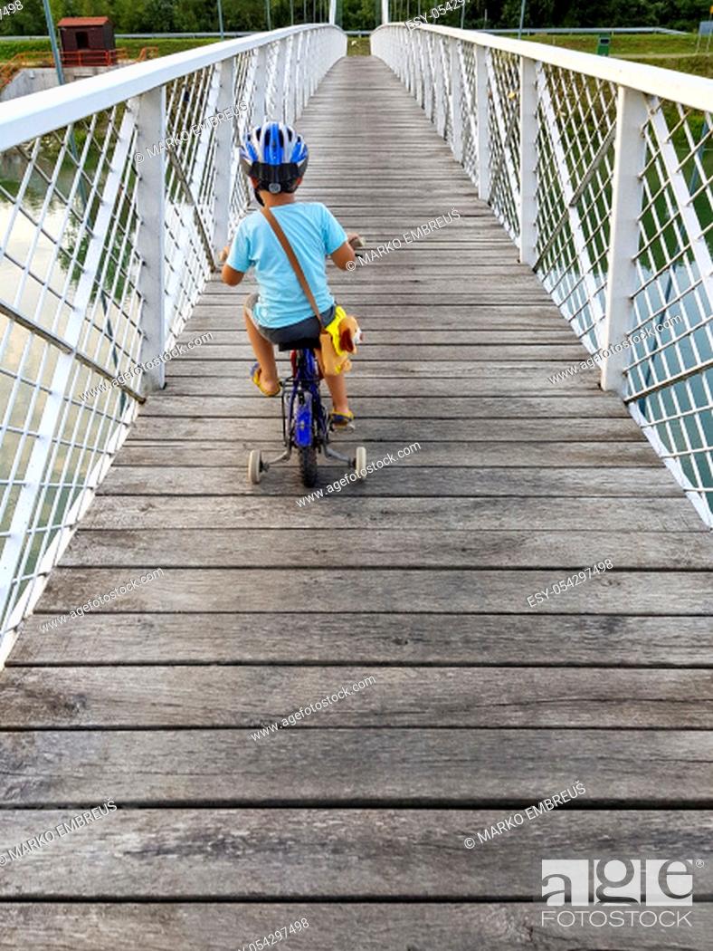 Imagen: A boy with bicycle on a bridge. The boy has bicycle helmet. White suspension bridge over the river Drava.