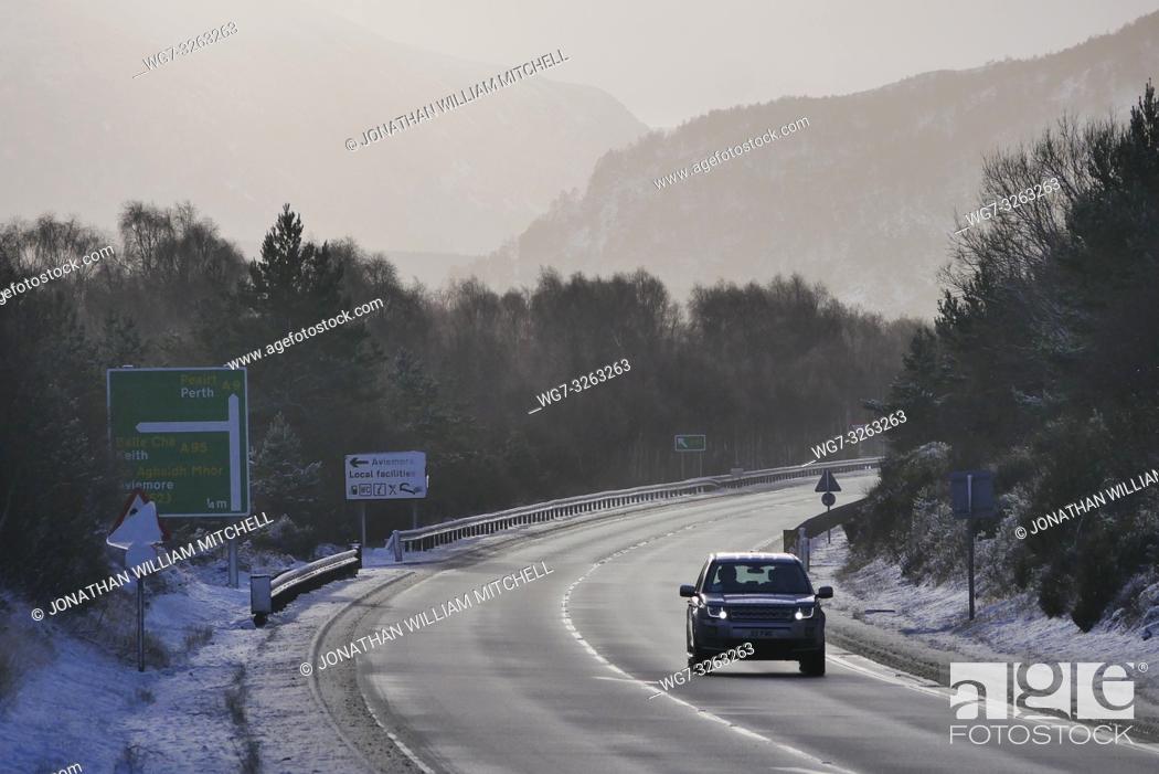 Stock Photo: AVIEMORE, SCOTLAND, UK - 17 Jan 2019 - A driver braves the A9 amid a snowy landscape showing the snowy mountains of the Cairngorms near Aviemore Scotland UK.