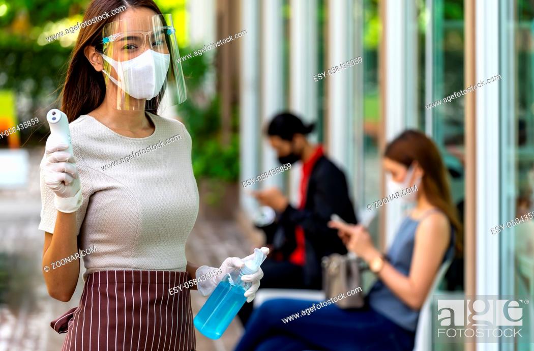 Stock Photo: Portrait attractive asian waitress wear face mask and shield hold thermometer and alcohol gel sanitizer with background of social distancing customer waiting in.