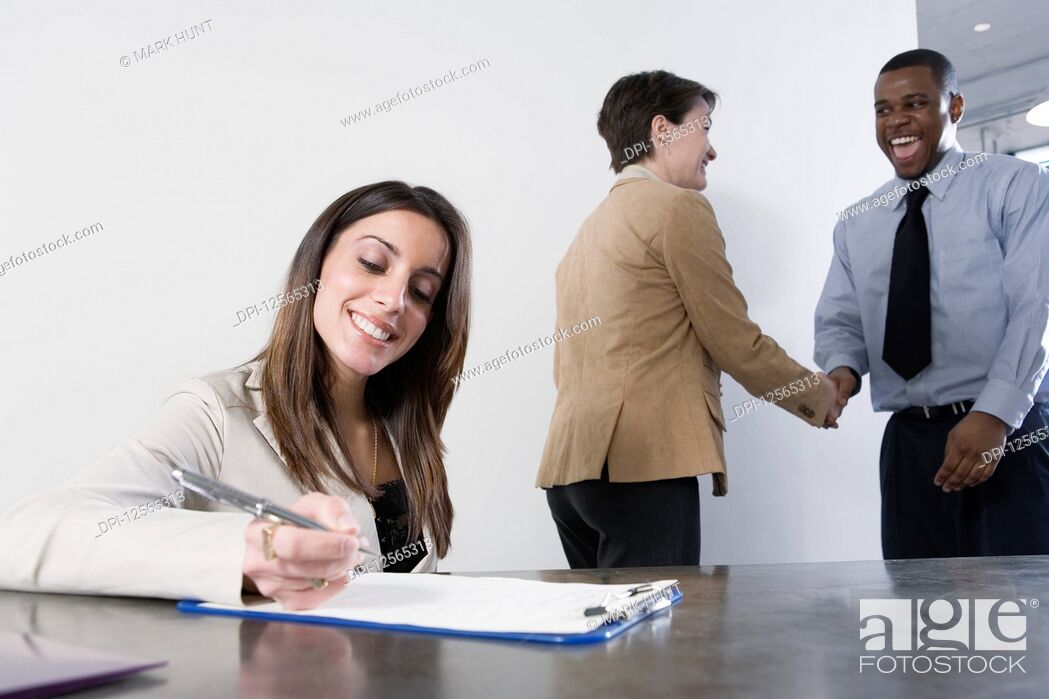 Stock Photo: Business woman writing with business colleagues shaking hands in background.