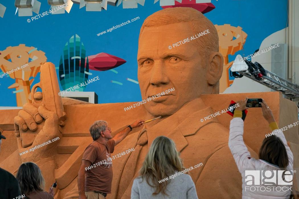 Stock Photo: 22 September 2021, Saxony-Anhalt, Weißenfels: Artist Benno Lindel is putting the finishing touches to his sand sculpture on the theme of ""James Bond"" in a.