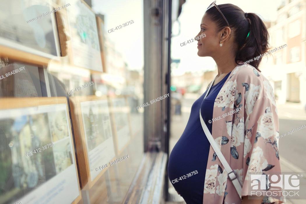Stock Photo: Pregnant woman browsing real estate listings at urban storefront.