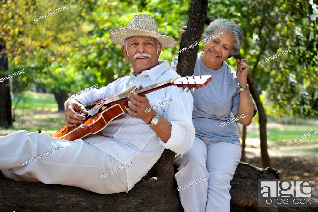 Stock Photo: Smiling senior man with woman having fun at park while playing guitar.