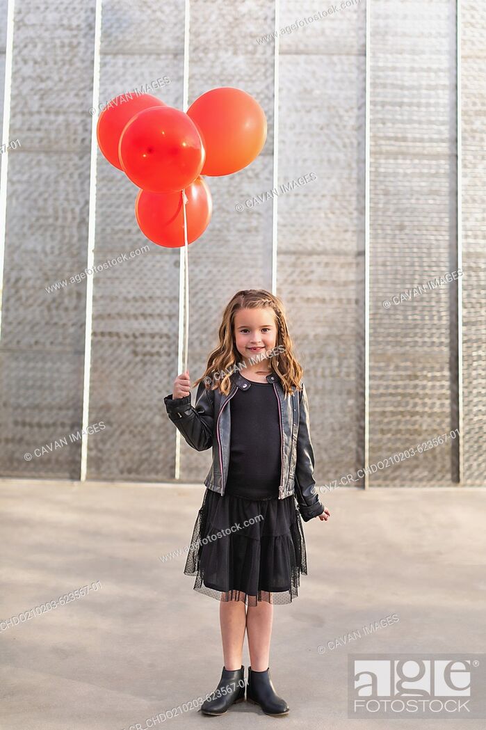 Stock Photo: Young girl holding red balloons in front of a metal wall.