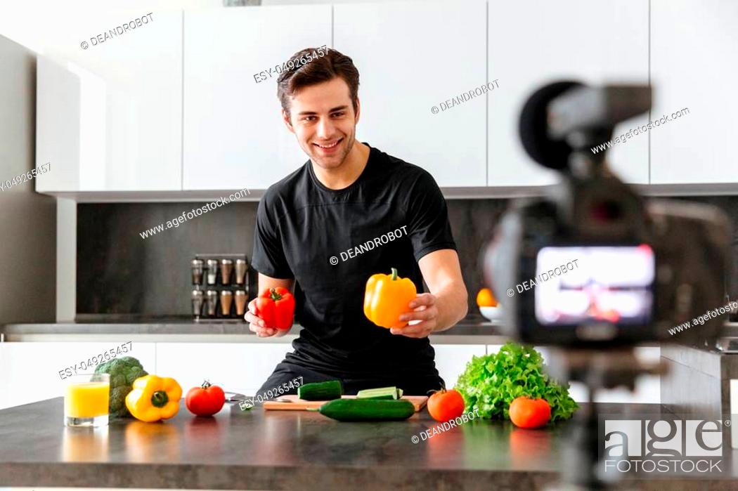 Stock Photo: Cheerful young man filming his video blog episode about healthy food cooking while standing at the kitchen.