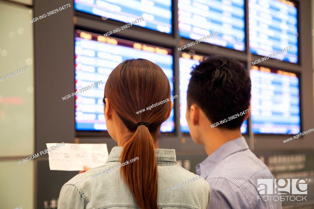 Stock Photo: Two travelers looking at flight departure screens at airport.