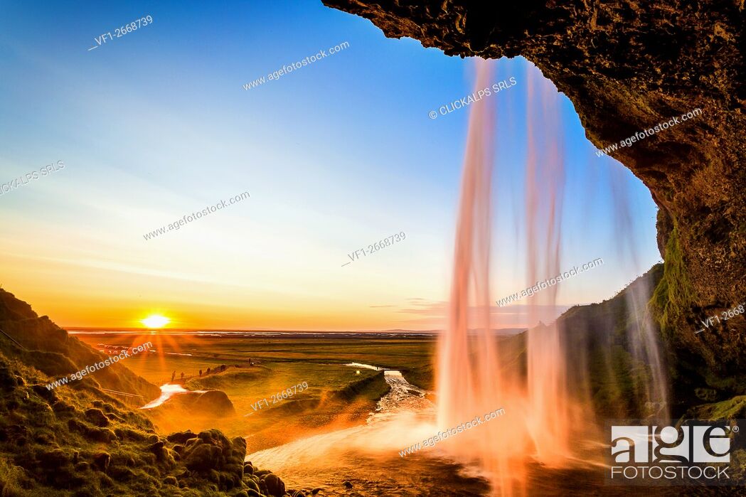 Stock Photo: Iceland landscape, Seljalandsfoss waterfall at sunset, picture taken from behind the fall with sunburst.