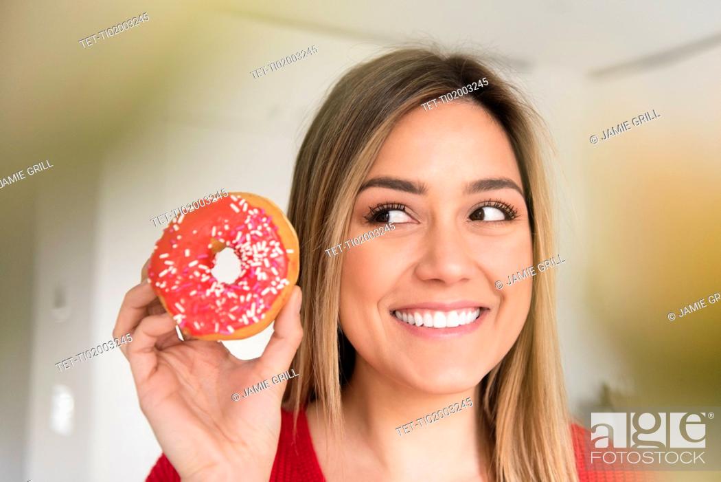 Stock Photo: Smiling young woman holding donut with pink icing.