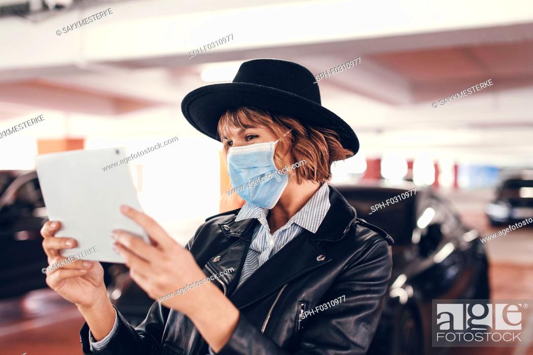 Stock Photo: Young urban woman in mask and hat using tablet.