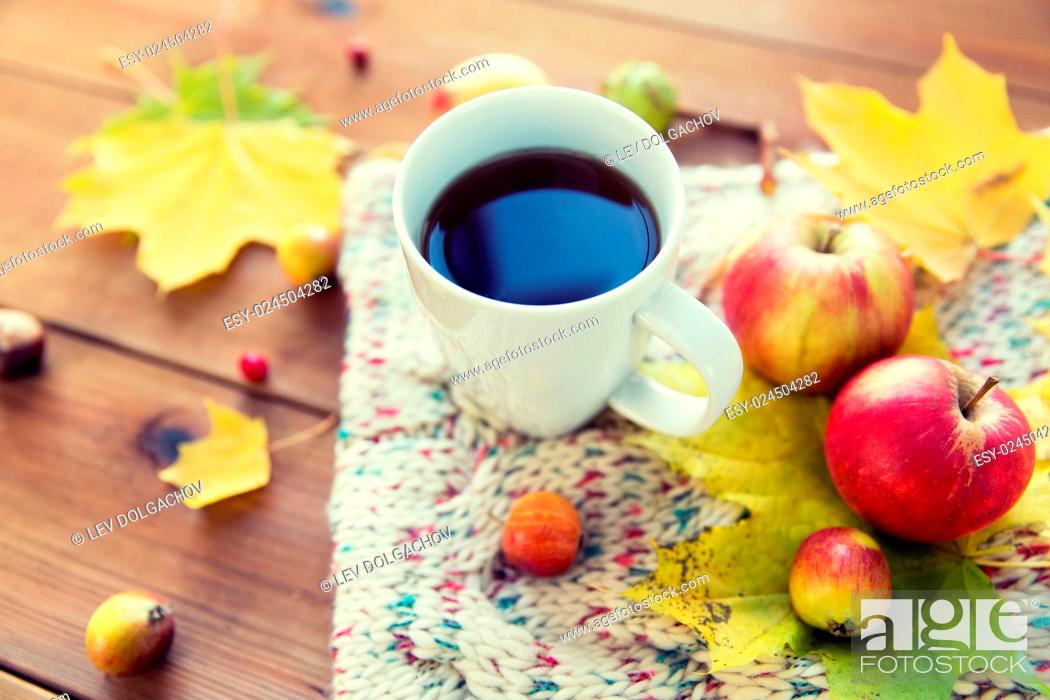 Photo de stock: season, drink and morning concept - close up of tea cup on wooden table with autumn leaves and scarf.