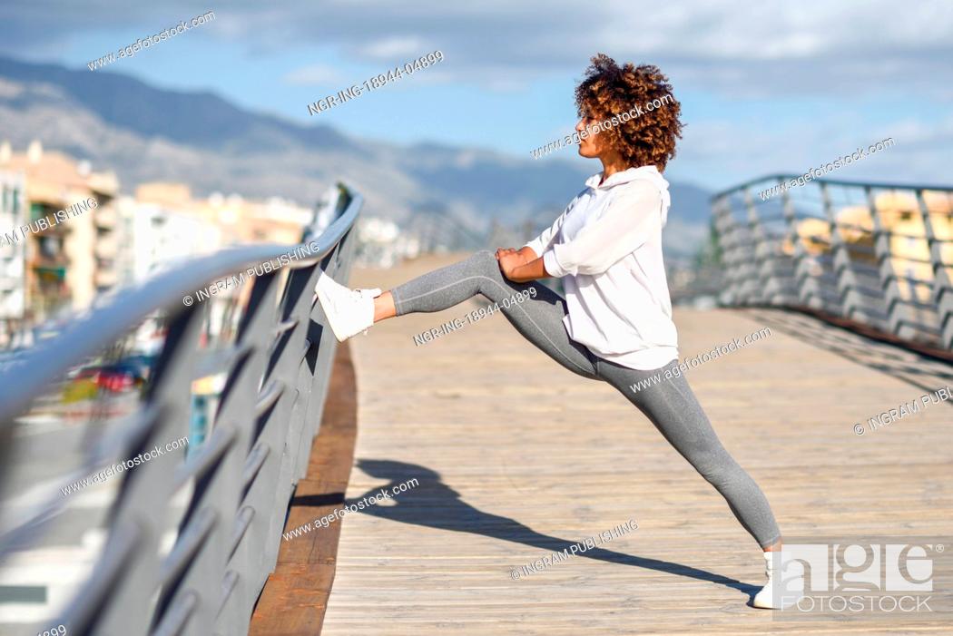 Stock Photo: Young black woman doing stretching after running outdoors. Girl exercising with city scape at the background. Afro hair.