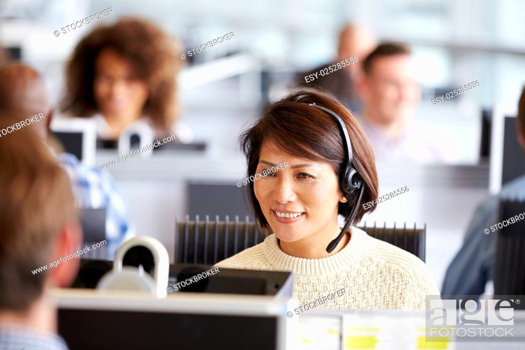 Stock Photo: Asian woman working in call centre, surrounded by colleagues.