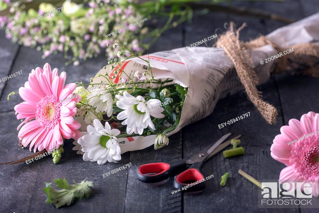 Stock Photo: Image about the activity of wrapping flowers with a bouquet of chrysanthemum packed in newspaper, surrounded by blooms and scissors.