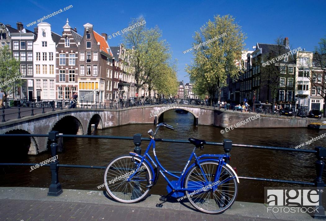 Stock Photo: Blue bicycle leaning against a railing on bridge with Keizergracht Canal running parallel and Leidsegracht perpendicular.