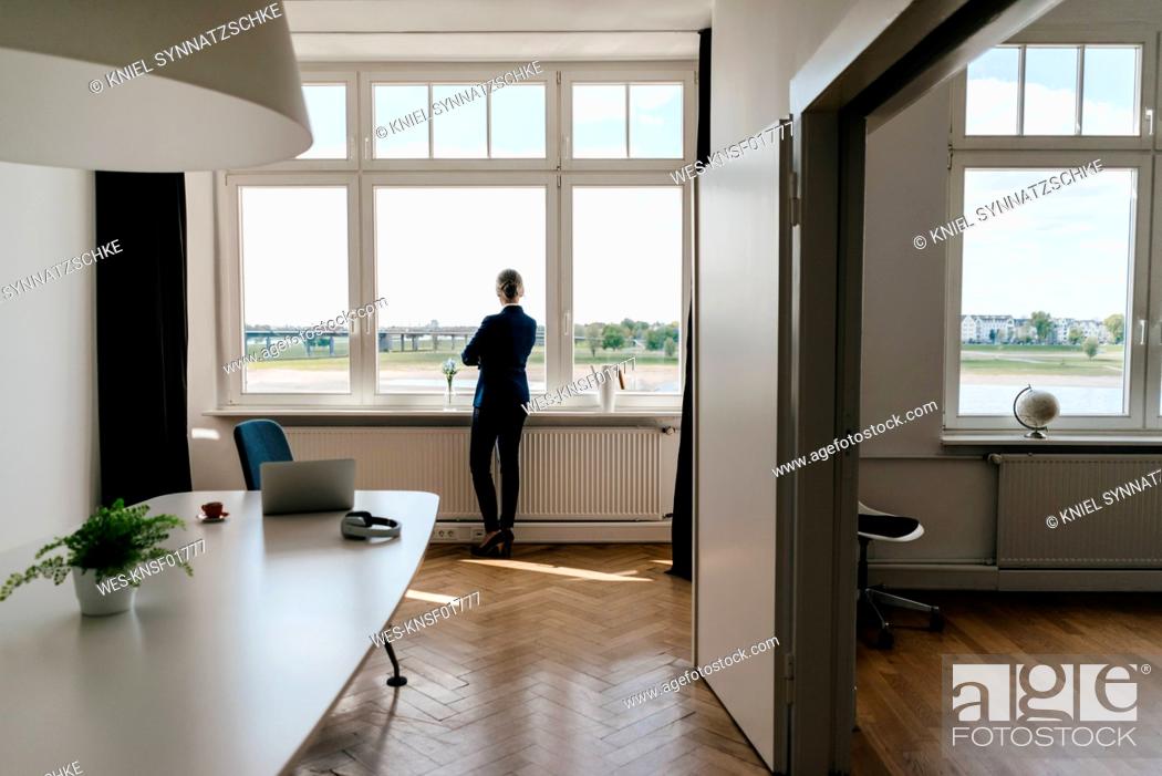 Stock Photo: Businesswoman standing in modern office looking out of window.