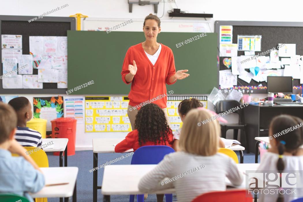 Stock Photo: Front view of a teacher teaching to elementary students in classroom at school with greenboard in background.
