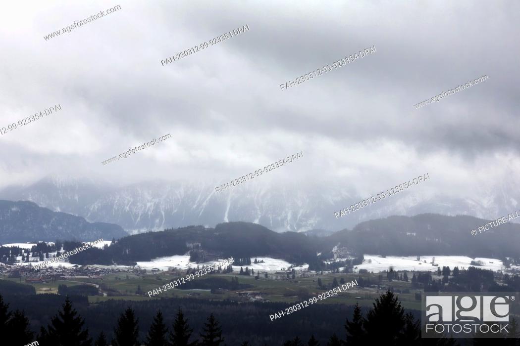 Stock Photo: 12 March 2023, Bavaria, Stötten: The foothills of the Alps, which are partly covered with snow, appear cloudy. Photo: Karl-Josef Hildenbrand/dpa.