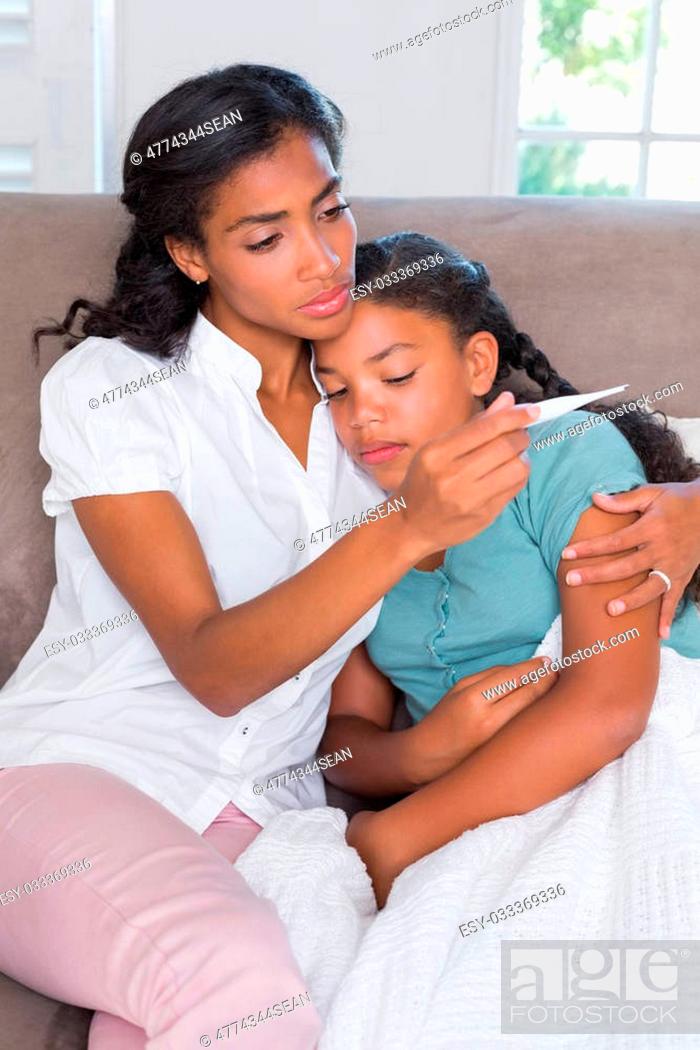 Stock Photo: Concerned mother taking her daughters temperature at home in living room.