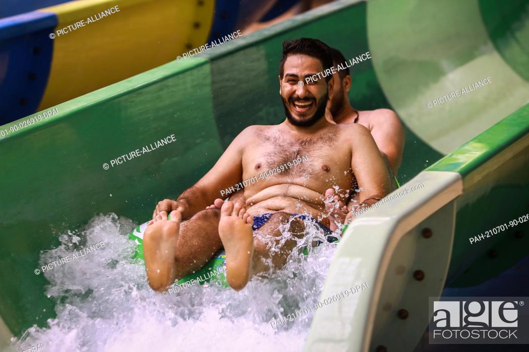 Stock Photo: 01 July 2021, Iraq, Baghdad: Two Iraqi men go down a water slide at the Baghdad Aqua Park amid an ongoing heatwave. Photo: Ameer Al Mohammedaw/dpa.