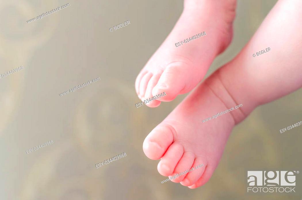 Stock Photo: Tiny little newborn daughter baby's feet close up sitting on her mother's hands at home, shallow focus on the toes, with a little blurred defocusing.