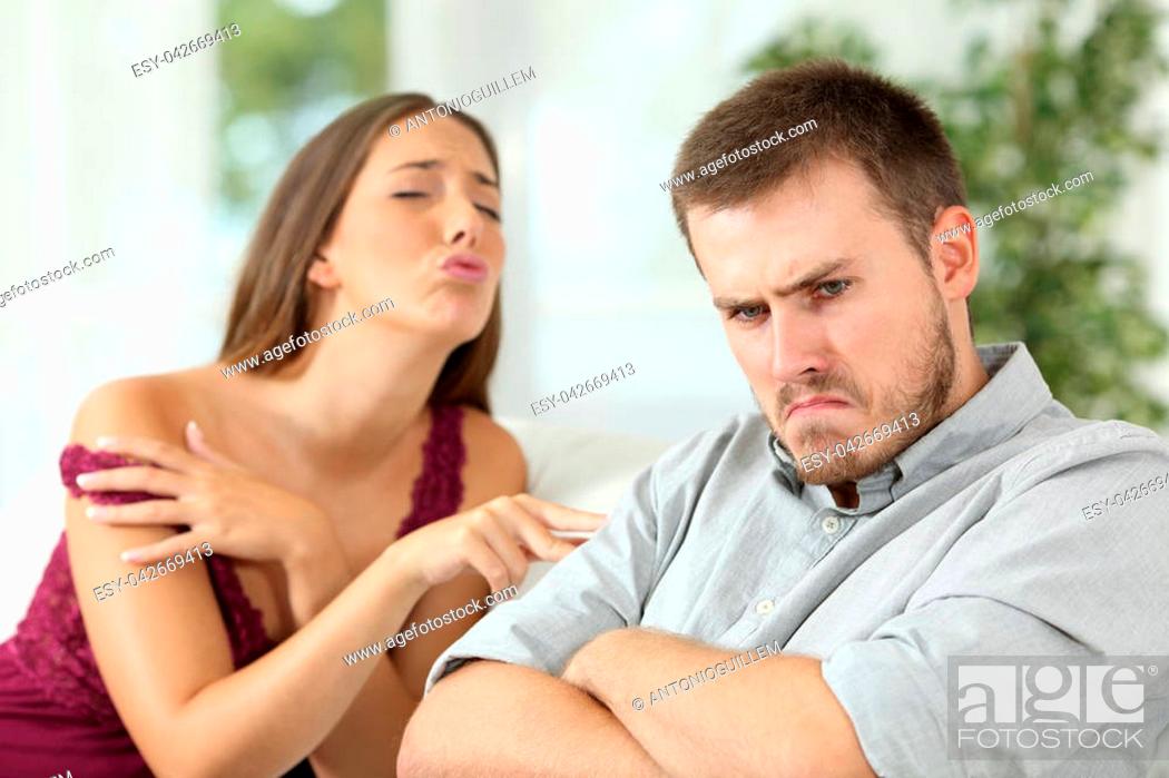 Stock Photo: Angry man rejecting a sex offer from his sexy girlfriend sitting on a couch in the living room at home.